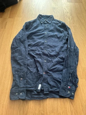 Mörkblå skjorta från Tommy Hilfiger - Klassisk mörkblå skjorta från Tommy Hilfiger i mjuk bomull. Skjortan har långa ärmar, knappar framtill och diskret broderad logga på bröstet. Perfekt till jeans eller chinos för en clean och enkel look.