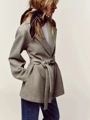 Grå omlottkappa från Zara med bälte - Helt Ny. Säljer en snygg grå kappa från Zara i omlottmodell med bälte i midjan. Jackan har klassisk krage, långa ärmar och är tillverkad i ett mjukt, stickat material som ger en chill och stilren vibe. Perfekt att slänga på sig över jeans eller klänning.