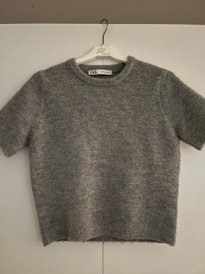 Grå stickad kortärmad tröja från ZARA - Säljer en mysig grå stickad tröja från ZARA med korta ärmar i storlek S. Den är använd ENDAST 2 gånger!