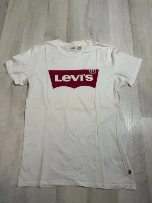 Levi’s T-shirt vit med röd logga – storlek XS – fint skick - Vit T-shirt från Levi’s med klassisk röd logga framtill. Tidlös modell som passar till det mesta – perfekt till vardag och skola.  Tröjan är använd men i fint skick, inga hål eller fläckar Storlek: XS Färg: Vit med röd logga  Från djur- och rökfritt hem.