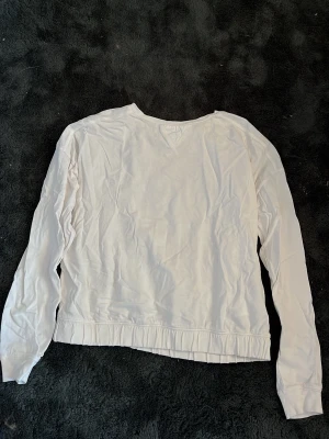 Vit långärmad sweatshirt/blus i bomull - En basic vit långärmad sweatshirt/blus i mjuk bomull. Tröjan har rund halsringning med dekorativ söm framtill och ribbad kant nedtill. Perfekt till chill dagar eller när du vill ha en clean look.