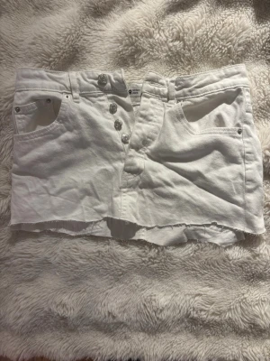 Vit jeanskjol från g perfect jeans  - Säljer en vit kort jeanskjol från g perfect jeans i storlek 36. Kjolen har rå kant nertill, fem fickor och knappar framtill. Klassisk sommar outfit . Perfekt till sneakers eller boots för en cool vardagsstil. Har klippt själv längst ner så kan vara lite ogemt 