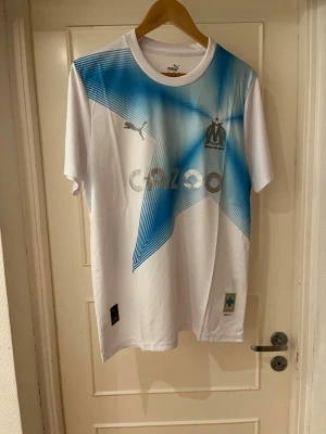 Marseille fourth kit 22/23  - Säljer en officiell Marseille matchtröja från Puma i storlek M. Tröjan är vit med en stor blå stjärna framtill, klubbmärke och Puma-logga. Tillverkad i lätt polyester som andas, perfekt för fotboll eller träning.