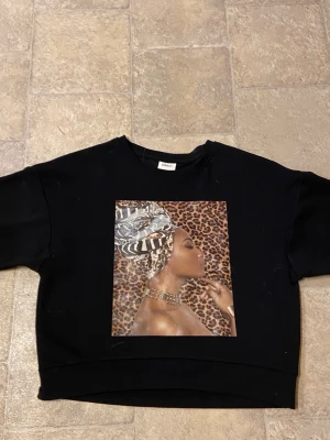 Svart t-shirt med leopardtryck från ONLY - Cool svart t-shirt från ONLY med ett stort tryck framtill som har leopardmönster och detaljer i brunt och beige. T-shirten är kortärmad och har en avslappnad passform. Perfekt för dig som vill sticka ut med ett unikt motiv.