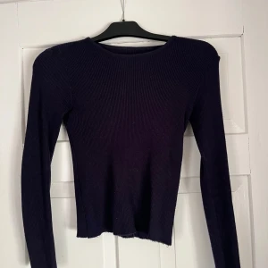 Mörkblå ribbad långärmad tröja - En svart, ribbad långärmad tröja med rund halsringning. Tröjan har en slim passform och är tillverkad i ett stretchigt material som sitter snyggt på kroppen. Perfekt att styla med jeans eller kjol för en enkel och clean look.