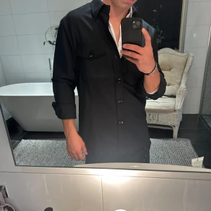 Svart overshirt från Suitsupply - Stilren svart overshirt från Suitsupply med klassisk krage, två bröstfickor med lock och knappar framtill🍁Skjortan har långa ärmar och är tillverkad i ett mjukt bomullstyg. Perfekt att bära öppen över en t-shirt eller med en skjorta under. Säljer för endast 849 kr!! Nypris ligger på flera tusen kr💫I nyskick utan några som helst skavanker och är i storlek M🙌