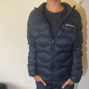 Svart dunjacka Peak Performance S - Säljer en svart dunjacka från Peak Performance i storlek S. Jackan har en klassisk pufferstil med diskret logga på bröstet och ärmen, dragkedja framtill och lång ärm. Perfekt för kalla dagar och riktigt skön att bära. Orginal pris 2000