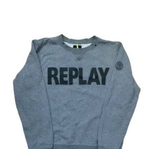 Grå sweatshirt från Replay - Snygg grå sweatshirt från Replay med stor svart logga framtill och rund hals. Tröjan har långa ärmar och mjukt material i bomullsblandning. Perfekt för en chill och stilren look. Replay-märke även på ärmen och nertill.
