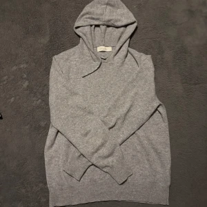 Grå hoodie i kashmir från Sayless - Mjuk och stilren grå hoodie från Sayless i kashmir. Klassisk modell med huva och dragsnören, ribbade muddar och lång ärm. Perfekt för dig som gillar en clean och enkel look med premiumkänsla.