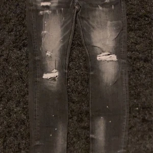 Grå slitna jeans Supply & Demand - Grå jeans från Supply & Demand med slitna detaljer och hål på benen. Modellen är smal och har en snygg tvätt med ljusare partier framtill. Klassisk femficksdesign och knapp med logga. Perfekta för en streetinspirerad look.