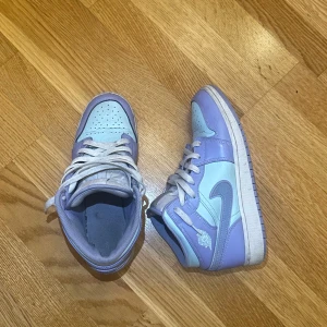 Nike Air Jordan 1 i lila och ljusblå - Säljer ett par Nike Air Jordan 1 sneakers i snygg lila och ljusblå färgkombination. Skorna har klassisk snörning, rund tå och vit sula. Ikonisk Jordan-logga på sidan och mjuk vadderad plös. Perfekta för dig som vill sticka ut med färg på fötterna.