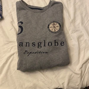 Grå sweatshirt från Henri Lloyd158 - Grå sweatshirt från Henri Lloyd med tryckt text och broderad patch på bröstet. Klassisk rund halsringning och avslappnad passform. Perfekt för en chill och sportig stil.