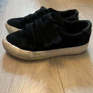 Svarta sneakers i manchester med kardborre - Svarta sneakers i manchestertyg med breda kardborreband och vit, tjock sula. Skorna har rund tå och en glansig detalj på hälen. Köpta förra året på zalando (even&odd) för 449kr. Storlek 38. Skorna är i fint skick, däremot är de smutsiga på sulorna så de behöver rengöras- inget som är svårt att få bort, men inte heller något jag har orkat göra, därav priset 😊 