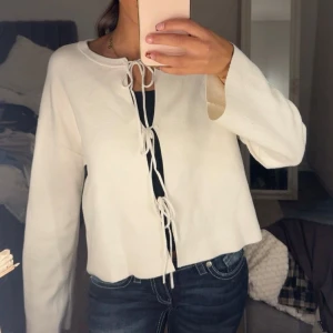 Vit kofta med snörning framtill - Säljer en vit kofta med långa ärmar och snygg snörning framtill. Koftan har en rak, lite boxig passform och är perfekt att slänga över ett linne eller t-shirt. Materialet känns mjukt och lätt, och den har en stilren look som passar till jeans. Snörerna är lite slitna.