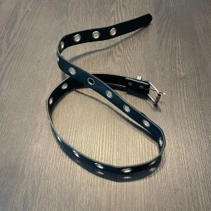 Svart bälte med silverhål - Säljer ett svart bälte i skinn med coola silverfärgade metallhål längs hela remmen. Bältet har en enkel silverfärgad spänne och passar perfekt till jeans eller kjol för en edgy look.