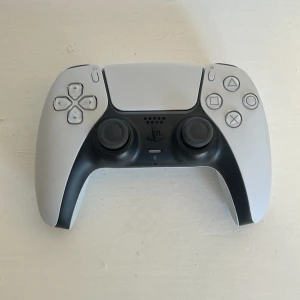 PlayStation 5 DualSense Controller - Snygg och modern PlayStation 5 DualSense handkontroll i vitt och svart. Kontrollen är i mycket gott skick med minimalt slitage, alla knappar och joysticks ser ut att fungera perfekt. Perfekt för gaming med avancerad haptik och adaptiva triggers.