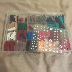 Färgglada lösnaglar i olika former - Säljer ett set med lösnaglar i flera färger som rött, blått, grönt, nude, vitt och svart. Naglarna kommer i olika former och längder, och medföljer gör även blommiga nagelstickers. Perfekt för dig som vill byta stil ofta och testa nya looks.