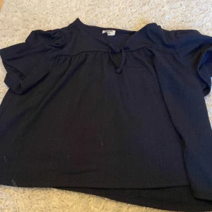 Mörkblå blus med knyt från Kappahl - Säljer en mörkblå blus från Kappahl i storlek 146/152. Blusen har korta ärmar, lätt puff vid axlarna och en söt knytning vid halsen. Den är tillverkad i ett mjukt, strukturerat tyg och har en avslappnad passform som är perfekt för en chill look. 40kr med frakt!👍