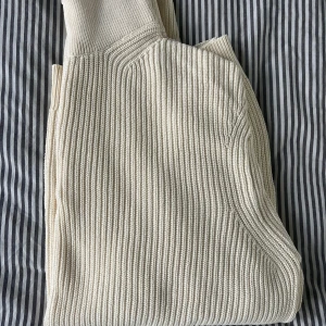 Ribbstickad kofta från EAST WEST - Ribbstickad creme vit zipup från EAST WEST med dragkedja framtill och hög krage. Snygg och enkel att matcha, perfekt för lager-på-lager. Mjuk och skön i stickad bomull, passar till allt. Storlek L och i topp skick, aldrig använd.