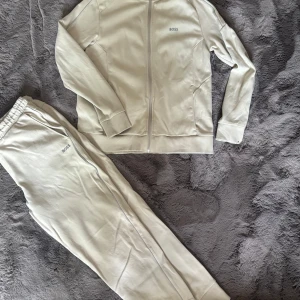 Beige ziptröja från BOSS - Snygg beige ziptröja från BOSS med diskret logga på bröstet. Tröjan har lång ärm, ribbade muddar och hel dragkedja framtill. Perfekt för en chill och stilren look. Materialet känns mjukt och skönt mot huden.