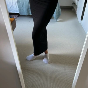 Svart långkjol i stretchigt tyg - Säljer en svart långkjol med tight passform och enkel design. Kjolen är figurnära och gjord i ett stretchigt material som sitter snyggt längs kroppen. Perfekt för dig som gillar en stilren och minimalistisk look. Den är lite åtdragen i sidorna som ger snygga veck längst med kjolen. Går även att ha som kort kjol om man vill