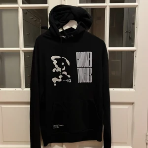 Svart Crooked Tongues hoodie med tryck - Svart hoodie från Crooked Tongues med stor vit grafisk print och text både fram och bak. Tröjan har huva med snörning och en klassisk känguruficka. Långa ärmar och cool streetstyle-vibe, perfekt för dig som gillar unika prints.