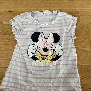 Randig Minnie Mouse t-shirt H&M - Söt t-shirt från H&M med rosa och vita ränder och ett stort tryck av Minnie Mouse på framsidan. T-shirten har korta ärmar och är gjord i mjuk bomull. Perfekt för dig som älskar Disney och vill ha en lekfull stil.