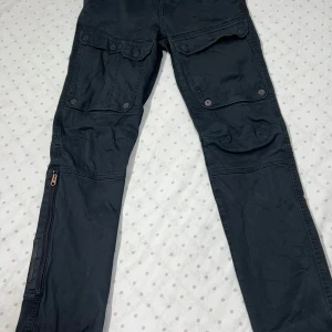 Svarta cargopants från G-Star RAW 28/32 - Svarta cargopants från G-Star RAW med stora fickor på benen och dragkedja längs nedre delen av benen. Byxorna har en cool streetstil och är gjorda i bomull för en skön känsla. Perfekta för dig som gillar funktionella och snygga byxor.