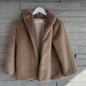 Beige pälsjacka från Dry Lake - Säljer en supermjuk och fluffig beige pälsjacka från Dry Lake. Jackan har en klassisk krage, helfodrad insida och stängs framtill. Perfekt för dig som vill ha en cozy och trendig look under kyliga dagar.