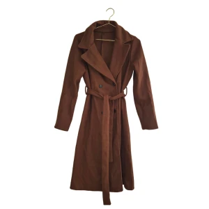 Brun trenchcoat med bälte - Snygg brun trenchcoat med klassisk krage och knytskärp i midjan. Jackan har dubbelknäppning framtill och långa ärmar. (jacka, kappa, trend, höstkappa) 