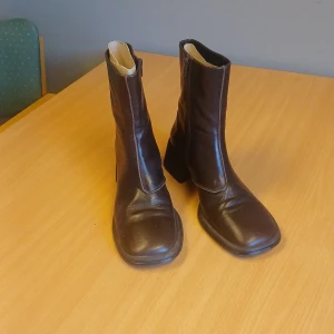 Bruna Vagabond boots i skinn - Snygga bruna boots från Vagabond i äkta skinn med fyrkantig tå och bred klack. Dragkedja på insidan för enkel påtagning. Perfekta för dig som gillar retrovibbar och vill ha ett statement-plagg till höst- och vinterlooken.