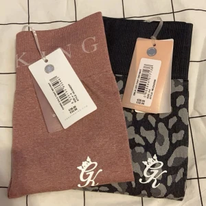 2 par Gym King leggings, rosa & leopard - Två par leggings från Gym King. Ena paret är i en snygg dämpad rosa färg med logga och bred resår i midjan, andra paret är svart med grått leopardmönster och samma logga. Båda har hög midja och är gjorda i stretchigt material som passar perfekt till träning.