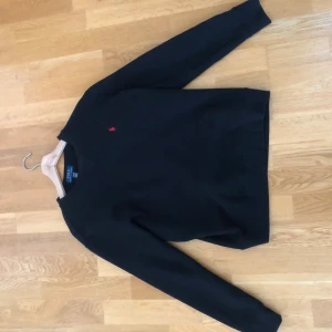 Svart tröja från Polo Ralph Lauren - Svart långärmad tröja från Polo Ralph Lauren med klassisk rund halsringning och röd broderad logga på bröstet. Tröjan är i mjuk bomull och har en enkel, stilren design som passar perfekt till jeans eller chinos. Storlek l i barn storlek mott finns på bild