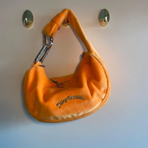 Orange axelväska Juicy Couture - Superfin axelväska från Juicy Couture i mjuk sammet med silvriga metalldetaljer i orange velour 🧡. Med väskan kommer samtliga accessoarer dvs plånbok (se bild 4), och en längre axelrem som båda går att knäppa på eller av! 