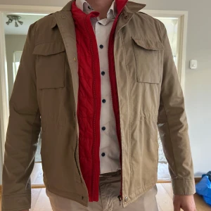 Beige jacka med  röd väst - Västjacka från Massimo Dutti i beige med två stora bröstfickor och dragkedja. Insidan har en snygga detaljer och en broderad logga. Medföljer en röd quiltad väst med dragkedja som kan användas separat eller tillsammans med jackan. Kan köpas separat vid intresse! Storlek XL