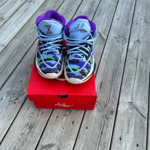 Nike Kyrie basket sneakers blå/lila - Färgstarka Nike Kyrie basket sneakers med coolt mönster i blått, lila, grönt och svart. Skorna har högt skaft, snörning och vit sula. Insidan är fodrad i lila och tungan har guldfärgade detaljer. Perfekta för dig som vill sticka ut på basketplanen.