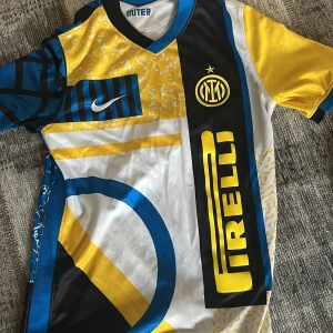 Inter Milan Nike fotbollströja L barn / 147 158 cm - Inter Milan matchtröja från Nike i storlek L. Tröjan har ett unikt grafiskt mönster i blått, gult, svart och vitt med klubbmärke och Pirelli-logga på bröstet. Tillverkad i lätt och ventilerande polyester, perfekt för fotboll eller att bära till vardags.