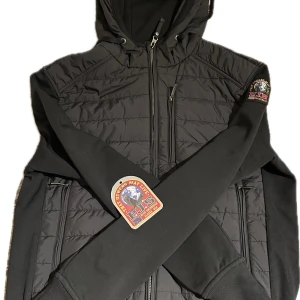 Parajumpers cardigan  - Exklusiv svart cardigan från Parajumpers – en perfekt mix av funktion och stil. Tillverkad i högkvalitativa material med stretch, dragkedja och klassisk Parajumpers-logo på ärmen. Snygg att bära som jacka under höst/vår eller som mellanlager under kallare dagar. En mångsidig och stilren investering! Välvårdad och redo att bäras direkt!