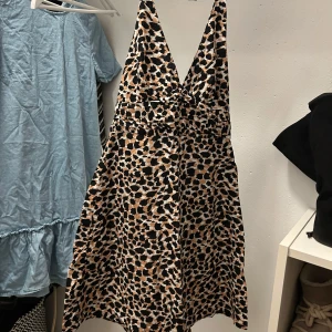 Leopardmönstrad omlottklänning - Snygg kort leopardmönstrad klänning med djup v-ringning och knyt i nacken. Klänningen har omlottkänsla och är tillverkad i ett glansigt, mjukt material som känns lyxigt. Perfekt för dig som vill sticka ut med ett djuriskt print.