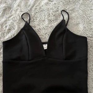 Svart linnetopp från Gina Tricot XS - Snygg svart linnetopp från Gina Tricot i storlek XS. Toppen har smala axelband och en djup v-ringning framtill. Enkel och stilren design som är lätt att matcha med olika outfits. Perfekt för dig som gillar minimalistisk stil.