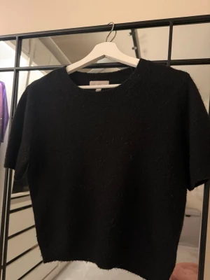 Svart stickad kortärmad tröja H&M - En svart stickad tröja från H&M med korta ärmar och rund hals. Enkel och stilren modell som passar perfekt till lager på lager eller för en clean look. Mjuk och skön kvalitet som känns lyxig mot huden.