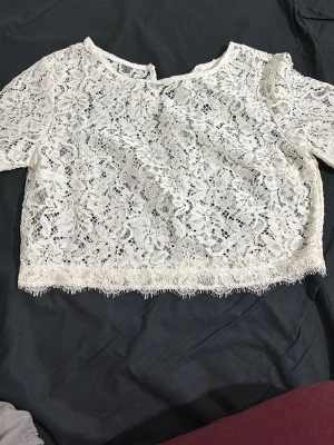 Vit spetsblus med blommönster - Säljer en vit blus i spets med blommigt mönster och korta ärmar. Blusen har en rund halsringning och är croppad med dekorativ kant nedtill. Materialet är tunt och genomskinligt, perfekt för lager-på-lager. Ingen synlig logga eller märke. Den är storlek M men passar som s och den är ganska kort. Har aldrig använt den innan eftersom den var ganska kort för mig, köpte den utomlands. Pris kan alltid diskuteras 