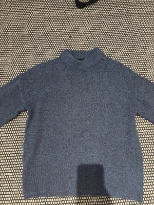Blå stickad tröja från 157, storlek M - Mysig blå stickad tröja från 157 i storlek M. Tröjan har en högre ribbad krage och långa ärmar. 