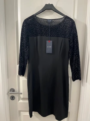 Svart leopardmönstrad klänning Armani Jeans - Snygg svart klänning från Armani Jeans med leopardmönstrad mesh upptill och på ärmarna. Klänningen har trekvartsärm och rak passform. Perfekt för dig som vill ha en stilren look med en twist. Materialet känns mjukt och följsamt.