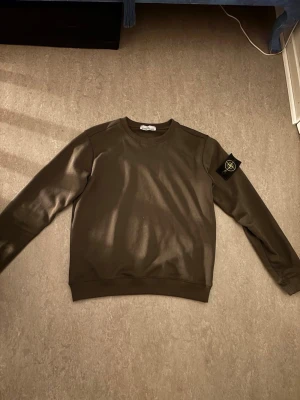 Mörkgrön sweatshirt från Stone Island - Säljer en mörkgrön sweatshirt från Stone Island med klassisk patch på vänster ärm. Tröjan har rund halsringning och långa ärmar. Tillverkad i mjuk bomull för skön känsla och stilren look.