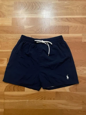 Marinblå badshorts Polo Ralph Lauren XL - Säljer ett par marinblå badshorts från Polo Ralph Lauren i storlek XL. Passar även M! Säljer i helt nytt skick då dem inte är använda! Hör av er vid eventuella fårgor! 😊