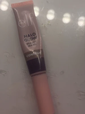e.l.f. Halo Glow Beauty Wand Contour - Säljer en e.l.f. Halo Glow Beauty Wand Contour i en mjuk tub med applikator. Färgen är en kall brun ton, perfekt för att skapa naturliga skuggor och definition i ansiktet. Enkel att blenda ut och ger ett snyggt glow. Praktisk för både nybörjare och proffs.