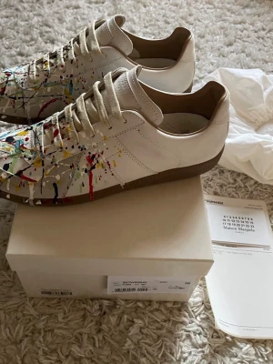 Maison margiela paint splatter - Säljer ett par Maison Margiela Paint Splatter sneakers i fint skick. Dessa har legat i garderoben inte använts något. Perfekt tillfälle för dig som vill ha något unikt i garderoben. Kvitto finns även, i form av äntehetsbevis. Kontakta mig om du är intresserad!