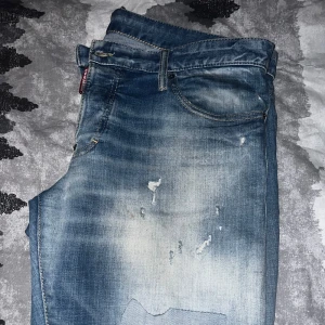 Blå jeans från Dsquared2 - Säljer ett par coola blå jeans från Dsquared2 med slitna detaljer och lappar. De har en klassisk femficksdesign och en knappgylf. Perfekta för en avslappnad stil. Använd några gånger men väldigt hållbara jeans så de är som helt nya!🤩