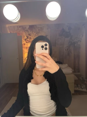 Svart kofta med volangkant - Säljer en svart kofta med snygga volangdetaljer längs kanten. Koftan är långärmad och har en smal passform som sitter snyggt över axlarna. Perfekt att slänga över ett linne eller topp för en chill men ändå uppklädd look.pris går att diskutera 